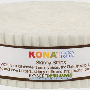 May include: A roll of Kona Cotton Solids Skinny Strips fabric. The off-white fabric is wrapped with a brown label that includes the text "Kona Skinny Strips" and product details. The strips are 1-1/2" wide.