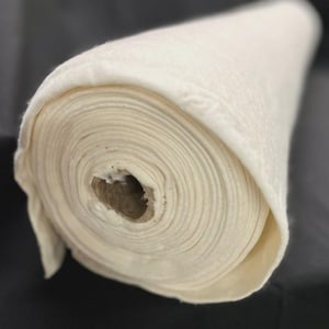 May include: A roll of off-white fabric, tightly wound, with visible layers. The fabric appears to be a soft, possibly natural material, with a slightly textured surface. The core of the roll is a brown cardboard tube.