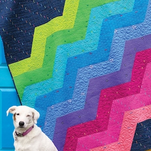 May include: A colorful chevron quilt pattern called "Wiley Way" by Sassafras Lane Designs. The quilt is made with a variety of bright colors, including blue, green, pink, and yellow. A white dog is sitting in front of the quilt.