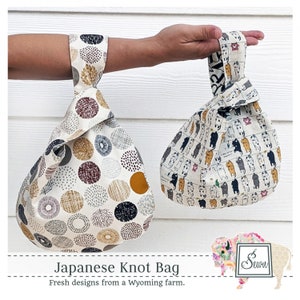 May include: Two Japanese knot bags, one with a white background and black, gray, and brown circles, and the other with a white background and black and white illustrations of cats. The bags are made of fabric and have a knotted handle.