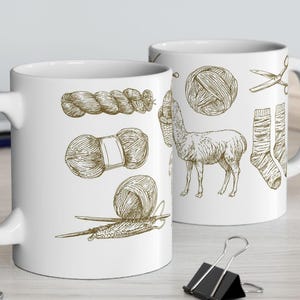 May include: Two white ceramic mugs with brown line drawings of yarn, knitting needles, scissors, a llama, and a sock. The mugs are on a light-colored surface with a laptop and office supplies in the background.
