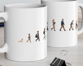 Puede incluir: Dos tazas de cerámica blanca con un gráfico que representa las etapas de la vida humana. El diseño muestra a un bebé gateando, seguido de niños, adultos y una persona mayor en silla de ruedas. Las tazas están sobre una superficie clara.