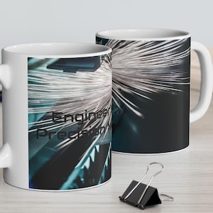 Puede incluir: Dos tazas de cerámica blanca con un diseño envolvente. Una taza muestra el texto "Engineered Precision" sobre una imagen abstracta azul y blanca. La otra taza muestra una imagen similar. Las tazas están sobre una superficie clara.