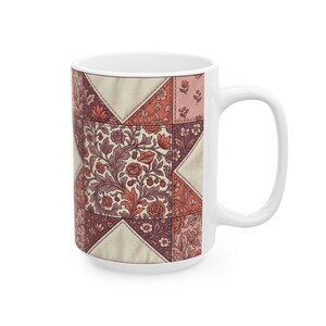 May include: White ceramic mug with a patchwork quilt design. The design features floral patterns in red, pink, and cream. The mug has a large handle and a wide base, suitable for hot drinks.
