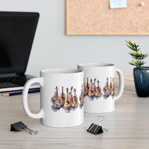 Könnte beinhalten: Zwei weiße Keramikbecher mit einem Aquarelldesign aus verschiedenen Streichinstrumenten. Die Instrumente sind in Braun-, Orange- und Blautönen gehalten.