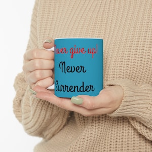 May include: A blue ceramic mug with the text "Never give up! Never Surrender" in black and red lettering.