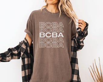May include: A brown t-shirt with the text "BCBA" repeated five times in white.