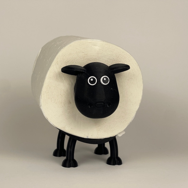 Puede incluir: Un porta rollo de papel higi&eacute;nico con forma de oveja en blanco y negro. La oveja tiene la cara negra con ojos blancos y nariz negra. El rollo de papel higi&eacute;nico es blanco y se mantiene en su lugar por el cuerpo de la oveja.