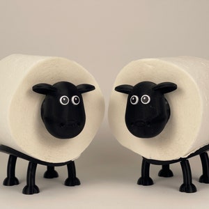 Puede incluir: Dos rollos de papel higi&eacute;nico blancos con caras y patas de ovejas negras. Las ovejas tienen ojos y narices negros.