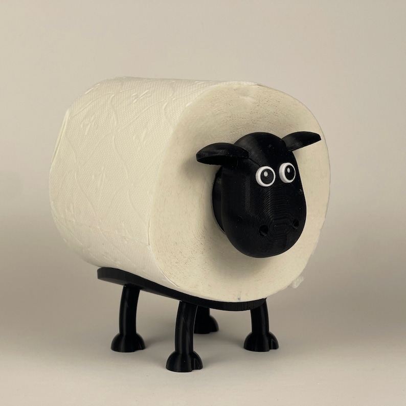 Puede incluir: Un porta rollo de papel higi&eacute;nico blanco con forma de oveja negra con grandes ojos blancos. La oveja tiene cuatro patas negras y una cara negra.