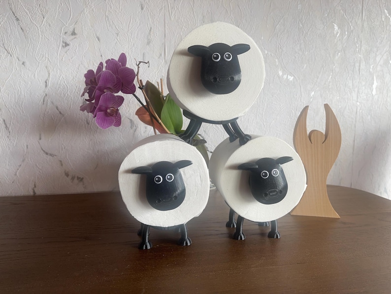 Puede incluir: Tres porta rollos de papel higi&eacute;nico blancos con forma de oveja con caras y patas negras. Las ovejas est&aacute;n apiladas una encima de la otra.