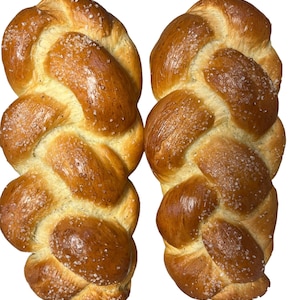 Op de afbeelding: Twee gevlochten broden met een lichtbruine korst en een snufje zout erop.