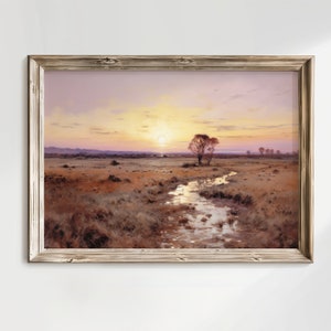 Könnte beinhalten: Ein gerahmtes Gemälde, das eine Landschaft mit einem Bach darstellt, der sich durch ein Feld schlängelt und auf einen fernen Sonnenuntergang zuführt. Der Himmel ist in sanftem Lila und Rosa gehalten, mit einer strahlend gelben Sonne, die durch die Wolken lugt. Zwei Bäume stehen in der Nähe des Baches, ihre Äste ragen in den Himmel.