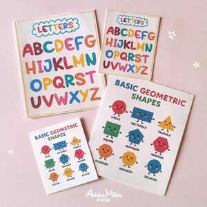Miniature educational flashcards featuring colorful alphabet letters and basic geometric shapes with cute faces, designed for dollhouse classrooms, school crafts, or early learning play, displayed on a light pink background. By Aninka Miller Minis