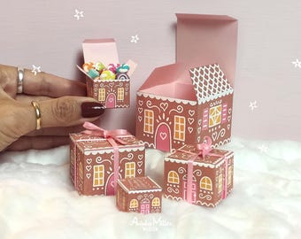 May include: Miniature gingerbread house and gift boxes with pink accents and bows. The boxes are decorated with white icing details, hearts, and windows. One box is open and filled with colorful candies.