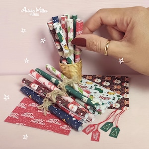 May include: Miniature Christmas craft supplies, including rolled paper, gift tags, and wrapping paper. The rolls are decorated with festive patterns and tied with twine. A small woven basket holds some of the rolls.