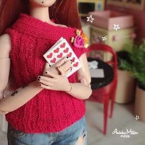 Miniature Valentines Day card set held by a doll in a cozy red sweater. Perfect for dollhouses, Valentines Day scenes, and miniature lovers. Features tiny cards with heart patterns, ideal for 1:6 scale or 1:12 scale doll displays