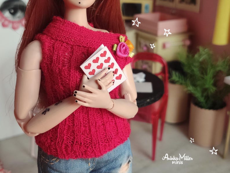 Miniature Valentines Day card set held by a doll in a cozy red sweater. Perfect for dollhouses, Valentines Day scenes, and miniature lovers. Features tiny cards with heart patterns, ideal for 1:6 scale or 1:12 scale doll displays