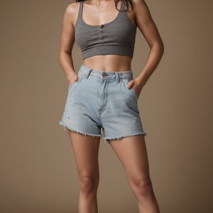 May include: A woman wearing a gray tank top with a button closure and light blue denim shorts with frayed edges.