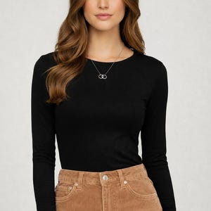 May include: A black long-sleeve shirt paired with brown corduroy pants. A silver necklace with a double-circle pendant is visible. The model is wearing a casual outfit.