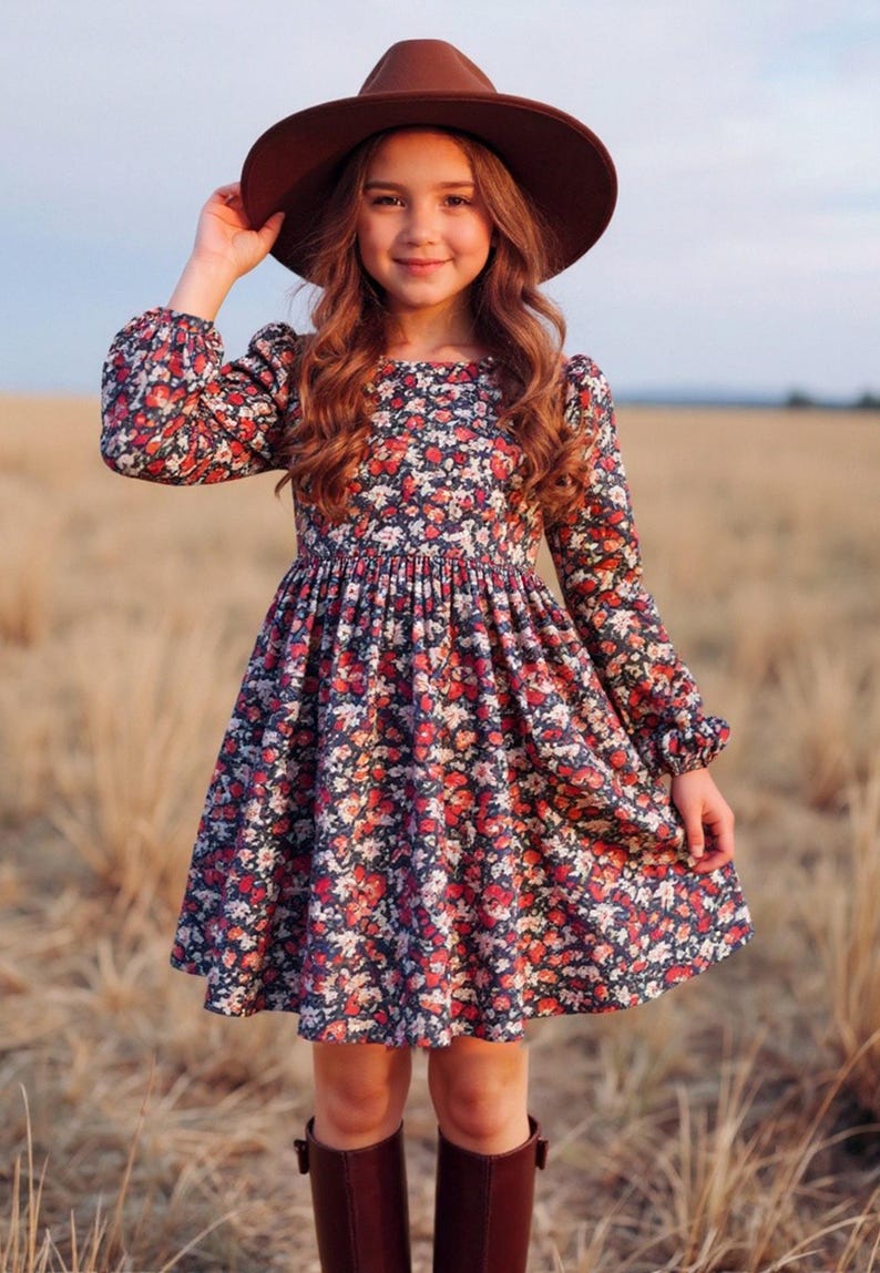 May include: A young person wearing a brown hat and a long-sleeved dress with a floral pattern in red, white, and pink on a navy blue background. The dress has a flared skirt and is paired with brown boots.