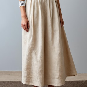 May include: A beige linen skirt with a high waist and pleats. The skirt is knee-length and has a flowy silhouette.
