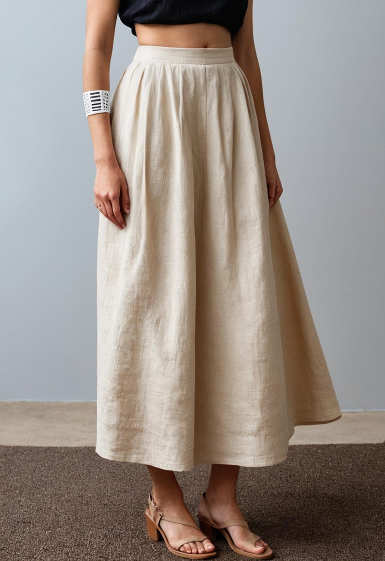 May include: A beige linen skirt with a high waist and pleats. The skirt is knee-length and has a flowy silhouette.