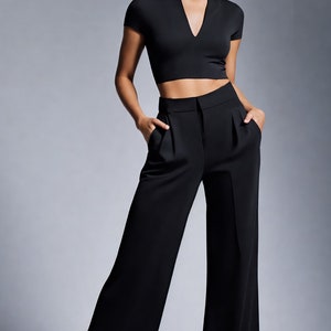 May include: A woman wearing a black cropped top and wide-leg black pants. She is wearing gold earrings.