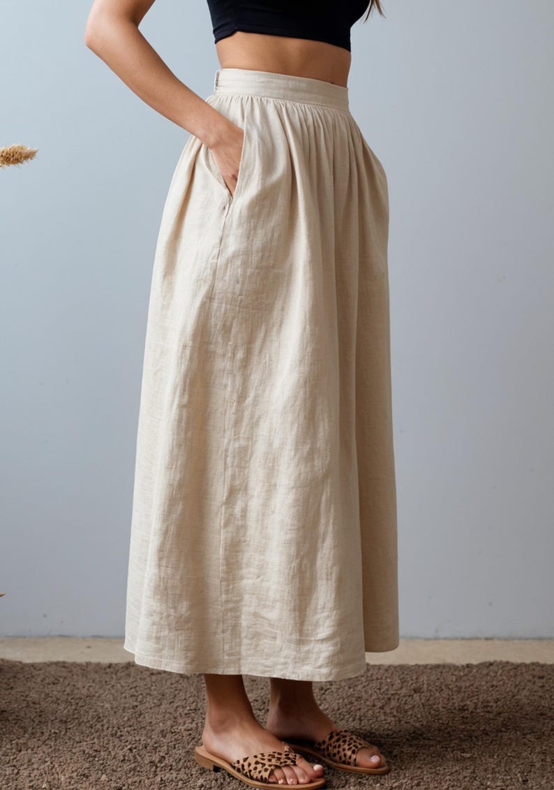May include: A beige linen skirt with a high waist and a gathered design. The skirt has pockets on the sides and falls to the mid-calf.