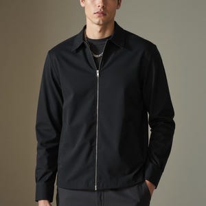 May include: A black zip-up jacket with a collared neckline. The jacket has a zipper closure and long sleeves.