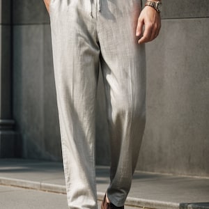 Peut inclure: Un pantalon en lin gris clair avec une taille &agrave; cordon. Le pantalon a un motif &agrave; rayures subtiles et est port&eacute; avec des chaussures en cuir marron.
