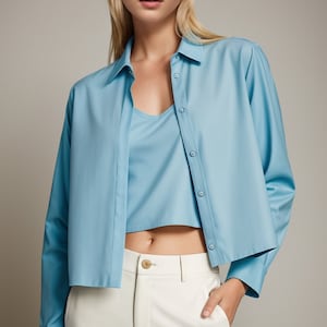 Op de afbeelding: Een lichtblauw getailleerd overhemd met lange mouwen en een wit tanktop eronder. Het model draagt een witte broek.