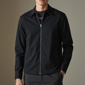 May include: A black zip-up jacket with a collared neckline. The jacket has a zipper closure and long sleeves.