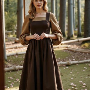 May include: A brown midi dress with a square neckline and a brown and tan color block design. The dress has long sleeves with puffed cuffs and a gathered skirt.