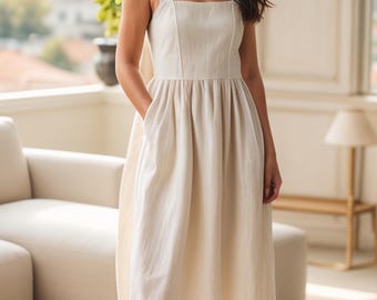 May include: A cream-colored midi dress with a square neckline and wide straps. The dress features a fitted bodice and a flared skirt with pockets. The model is wearing white flats. The dress is made of a textured fabric.