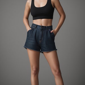 May include: A woman wearing a black crop top and dark blue denim shorts. She is standing with her hands in her pockets.