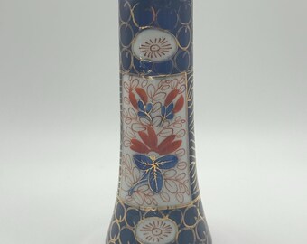 May include: A small, blue and white porcelain vase with a floral design. The vase has a flared base and a narrow neck. The floral design is in red, blue, and white.