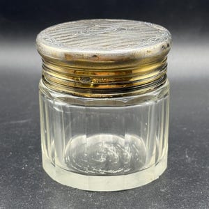 May include: A clear glass jar with a silver lid. The lid has a decorative design and is engraved with a monogram.