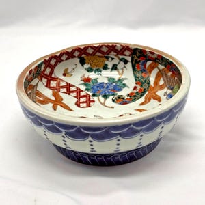 May include: A decorative ceramic bowl with a blue and white exterior and a detailed interior design. The interior features floral and geometric patterns in red, orange, yellow, and blue. The bowl has a round shape.