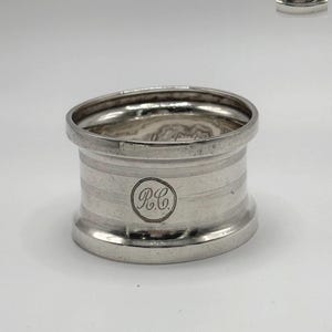 Puede incluir: Anillo de servilleta de plata con un diseño grabado circular que dice "R.C."