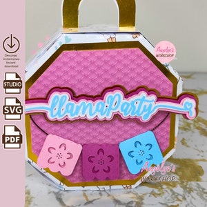 Op de afbeelding: Een roze en gouden achthoekige doos met een handvat. De doos heeft een gestikt patroon en een banner met de tekst "Llama Party". Er hangen drie kleurrijke papieren vlaggen aan de banner. De doos heeft een sticker met de tekst "Angelyc's Workshop".