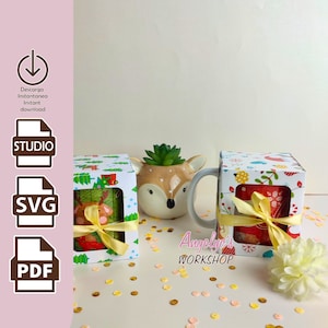 Könnte beinhalten: Zwei Weihnachts-Tassenboxen mit einem Fenster, um die Tasse im Inneren zu sehen. Die Boxen sind mit einem rot-grünen Muster und einem gelben Band verziert. Der Text "Angelic's Workshop" ist in der unteren rechten Ecke des Bildes sichtbar.