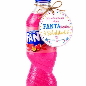 Könnte beinhalten: Eine Kunststoffflasche mit pinkfarbenem Fanta-Getränk und blauem Verschluss, an der ein rundes weißes Geschenketikett mit einer Schnur befestigt ist. Das Etikett ist mit bunten Punkten und dem Text Ich wünsche dir einen FANTAstischen Schulstart bedruckt.
