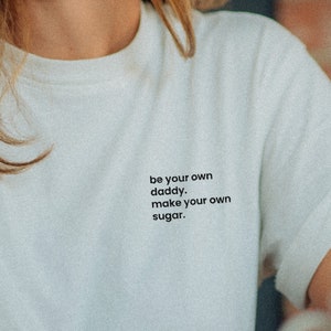 Könnte beinhalten: Weißes T-Shirt mit dem Text "be your own daddy, make your own sugar." auf der Vorderseite.