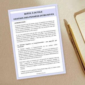 May include: A white paper with the title "BO&Icirc;TE &Agrave; OUTILS" and the subtitle "GESTION DES PENS&Eacute;ES INTRUSIVES" is displayed. The paper contains French text and is accompanied by a gold pen and a notebook.