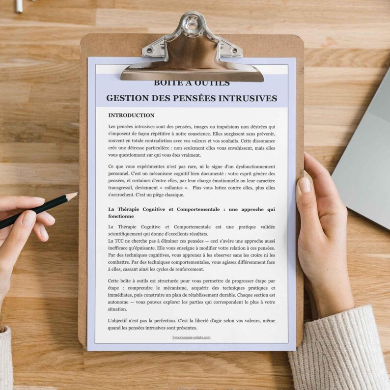 May include: A clipboard with a wooden base holds a document with French text. The document is titled "BOITE A OUTILS GESTION DES PENSEES INTRUSIVES" and includes text about intrusive thoughts and cognitive behavioral therapy.
