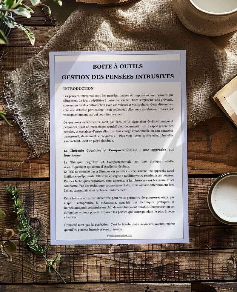May include: A printed document titled "BO&Icirc;TE &Agrave; OUTILS GESTION DES PENS&Eacute;ES INTRUSIVES" on a wooden surface. The document has text in French, with sections like "INTRODUCTION" and "La Th&eacute;rapie Cognitive et Comportementale".