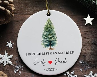 May include: White ceramic Christmas ornament with a watercolor painting of a green pine tree. The ornament reads "First Christmas Married Emily ♥ Jacob -2023-"