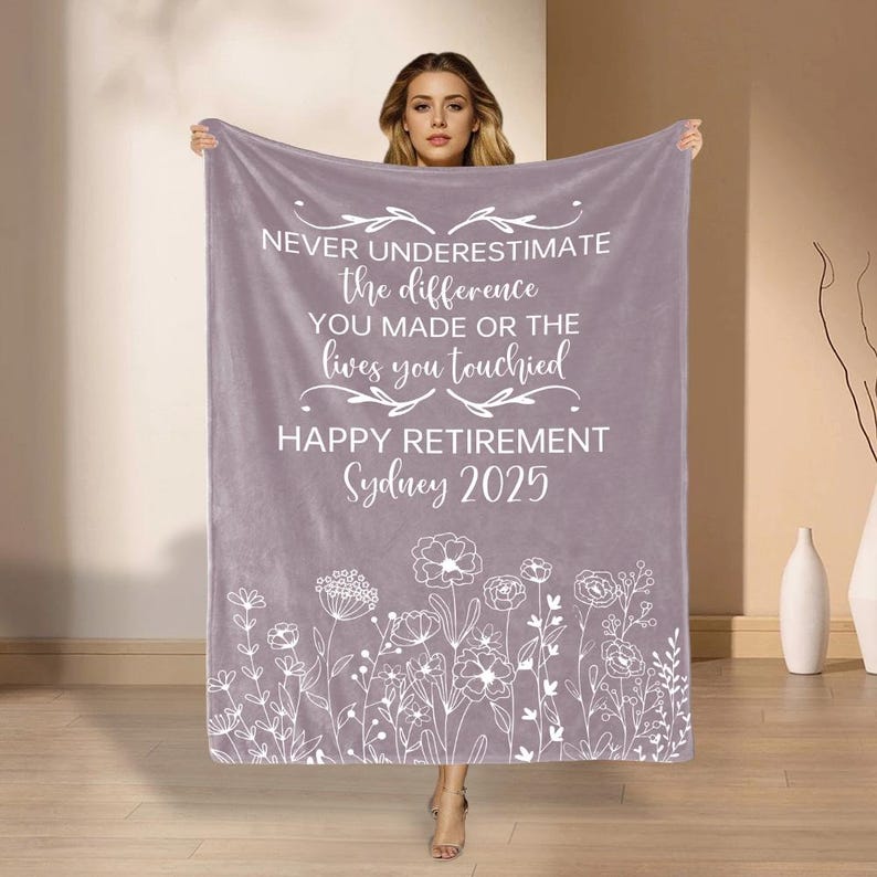 May include: A lilac-coloured blanket with white text. The text reads "NEVER UNDERESTIMATE the difference YOU MADE OR THE lives you touched HAPPY RETIREMENT Sydney 2025." A floral design decorates the bottom edge.