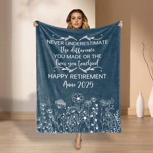 May include: A navy blue blanket featuring white floral patterns and the text "NEVER UNDERESTIMATE the difference YOU MADE OR THE lives you touched HAPPY RETIREMENT Anne 2025". The blanket is a soft, cozy item.